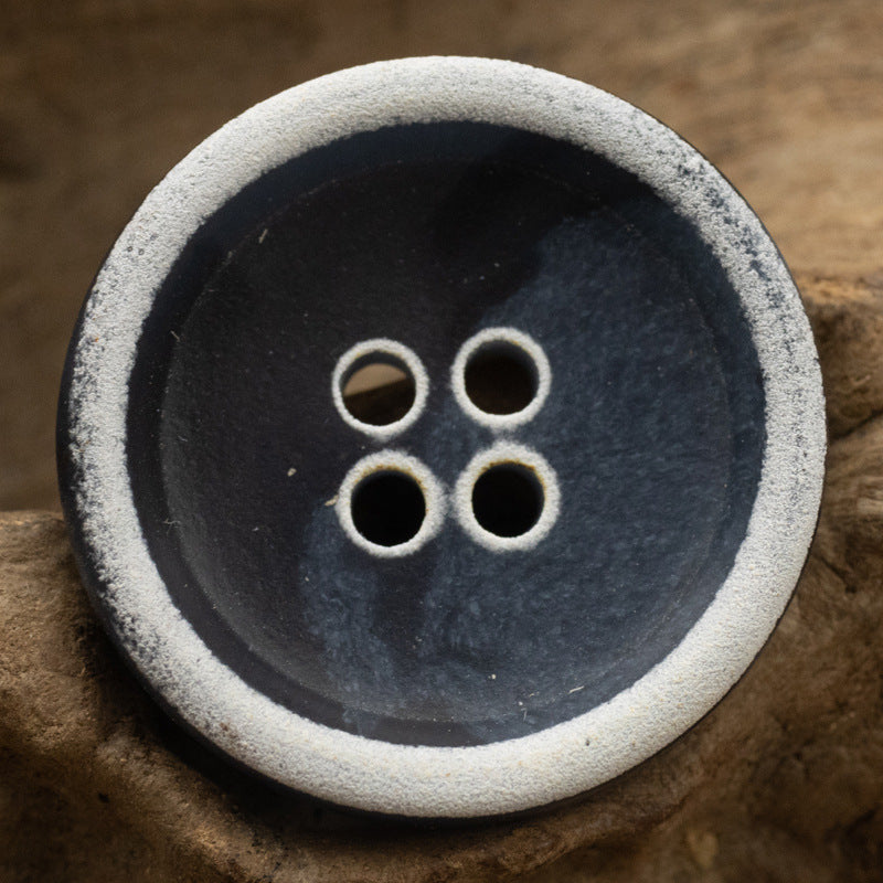 Dark blue urea button with four holes and light rim, close-up on wood