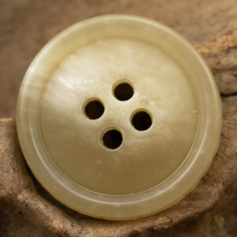 Round 4-hole urea coat button in pale ivory/cream with glossy surface