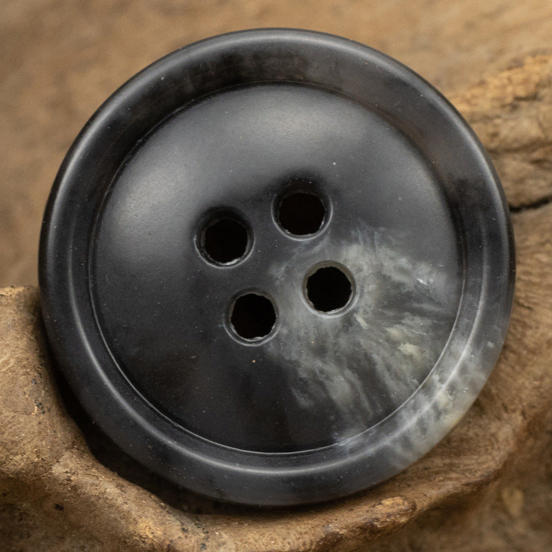 Round 4-hole urea coat button in matte dark gray/black with subtle texture