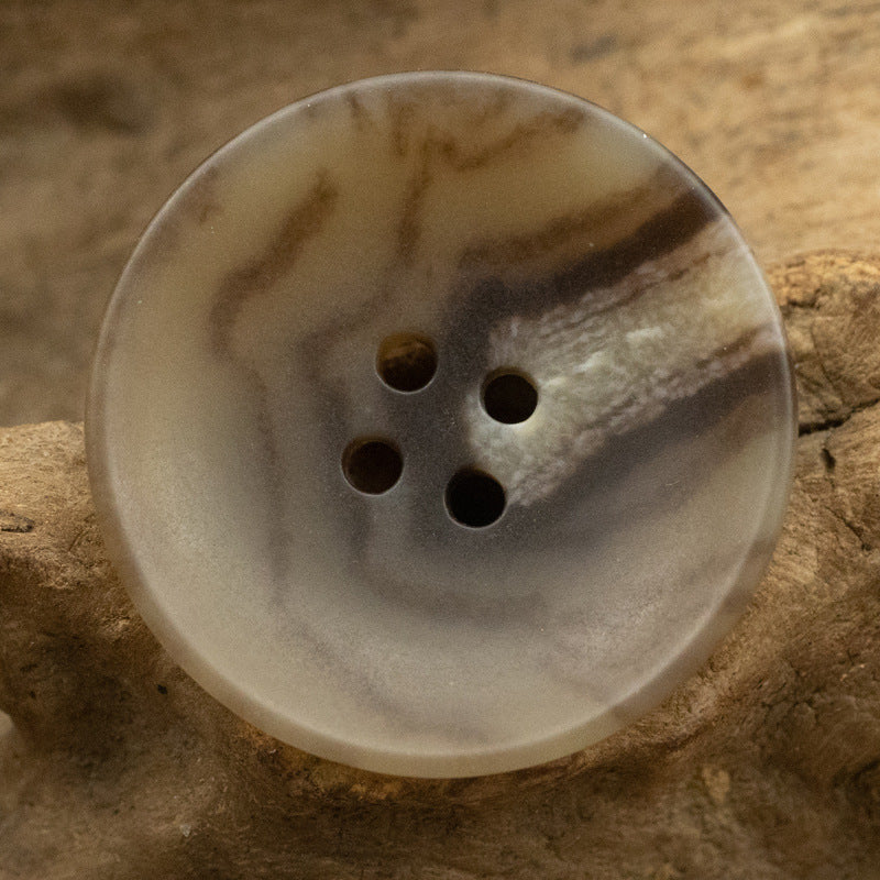 Translucent light beige round four-hole button with speckled pattern