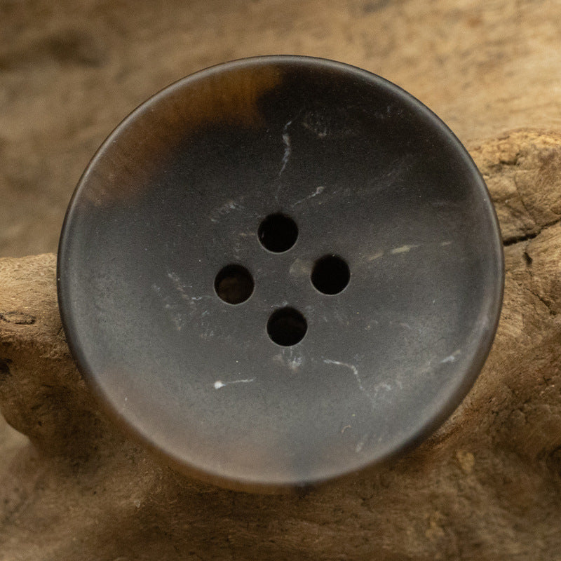 Dark gray round four-hole urea button with smooth surface and centered holes