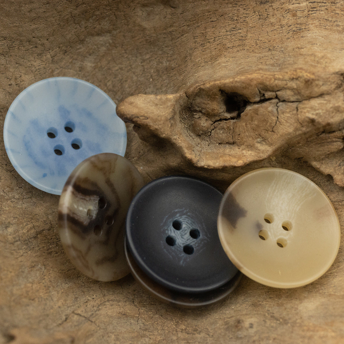 Round four-hole buttons in mixed colors: light blue, brownish, dark, and cream