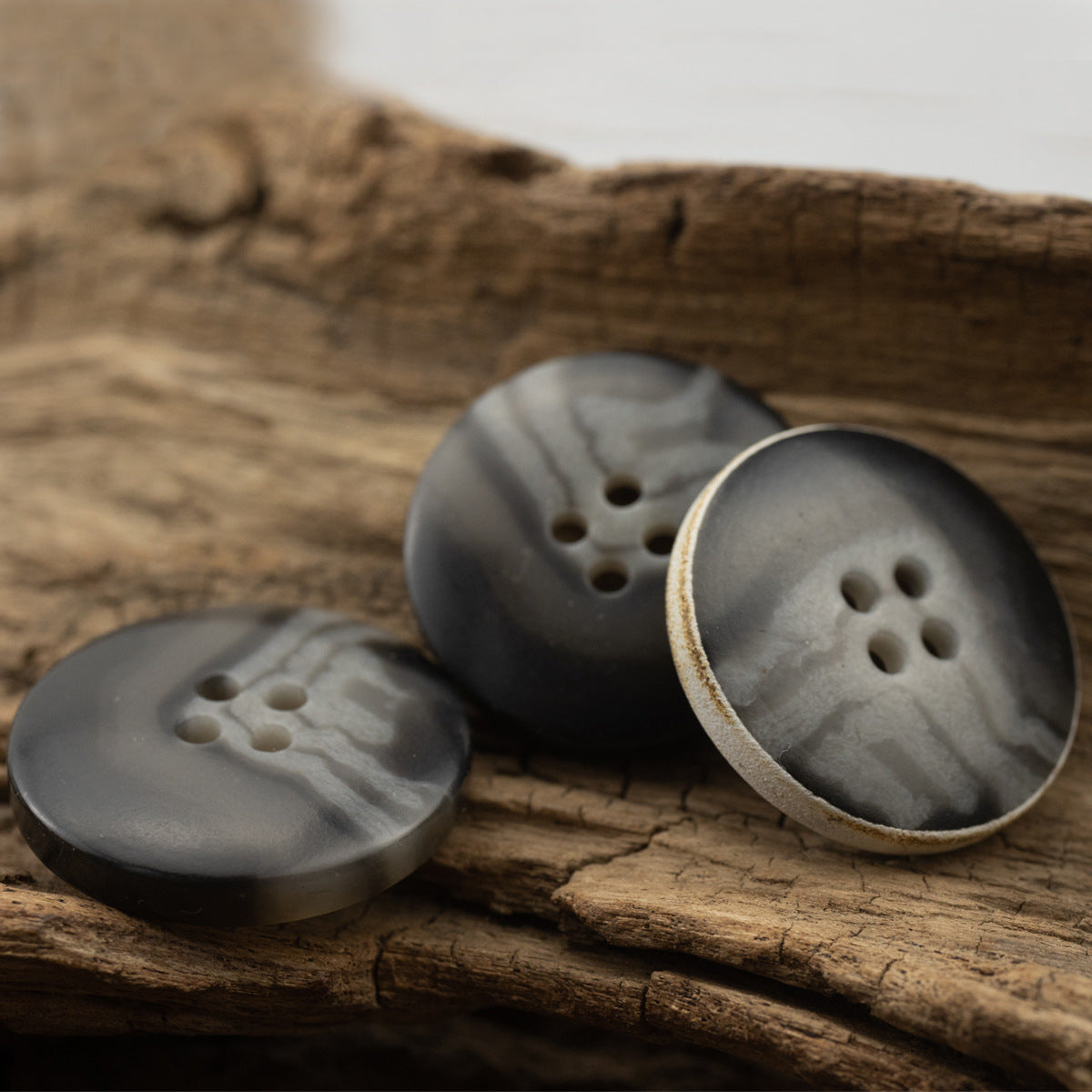 Set of dark gray-black textured buttons on wood, 4-hole design with burnt edges