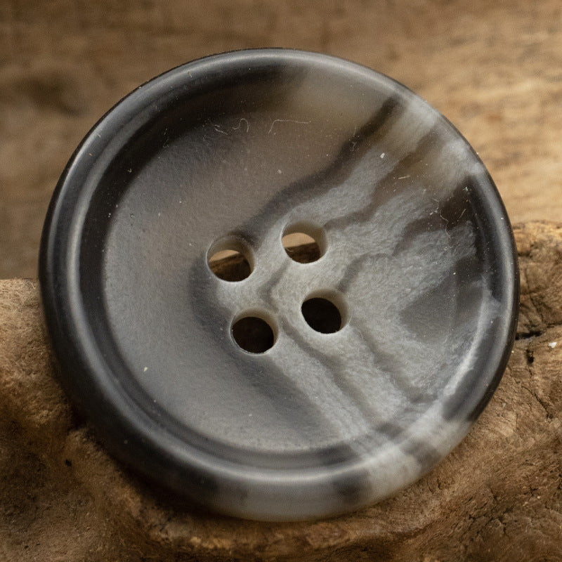Dark gray-black button with textured sheen and 4 holes, burnt-edge rim