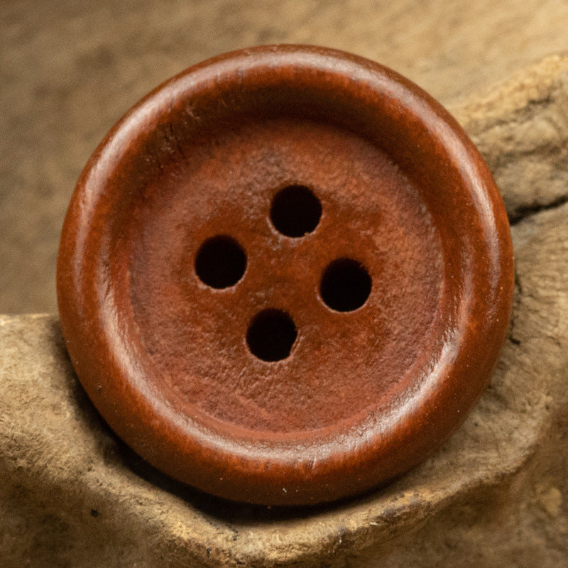 Brown vintage round wooden button with four holes and a smooth, carved rim