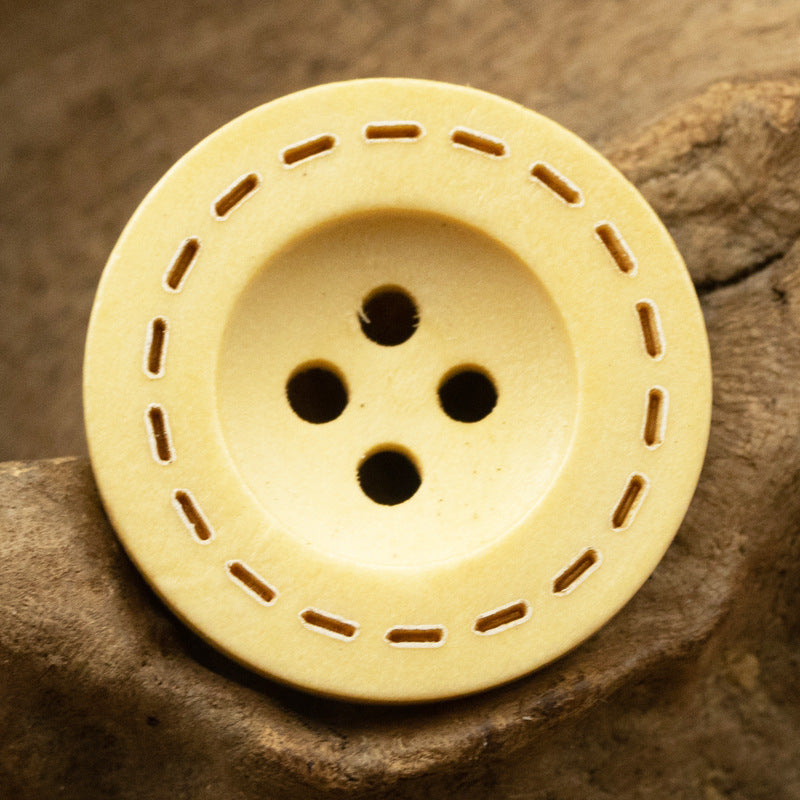 Yellow-lined round wooden button with four holes and decorative stitch cutouts