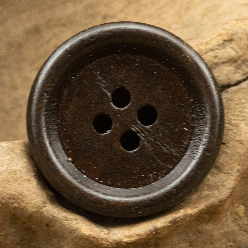 Dark vintage round wooden button with four holes and a textured surface