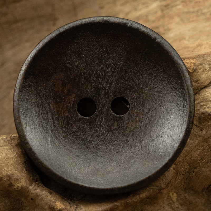 Two-hole dotted wood button, dark gray wood tone, bowl-shaped front view