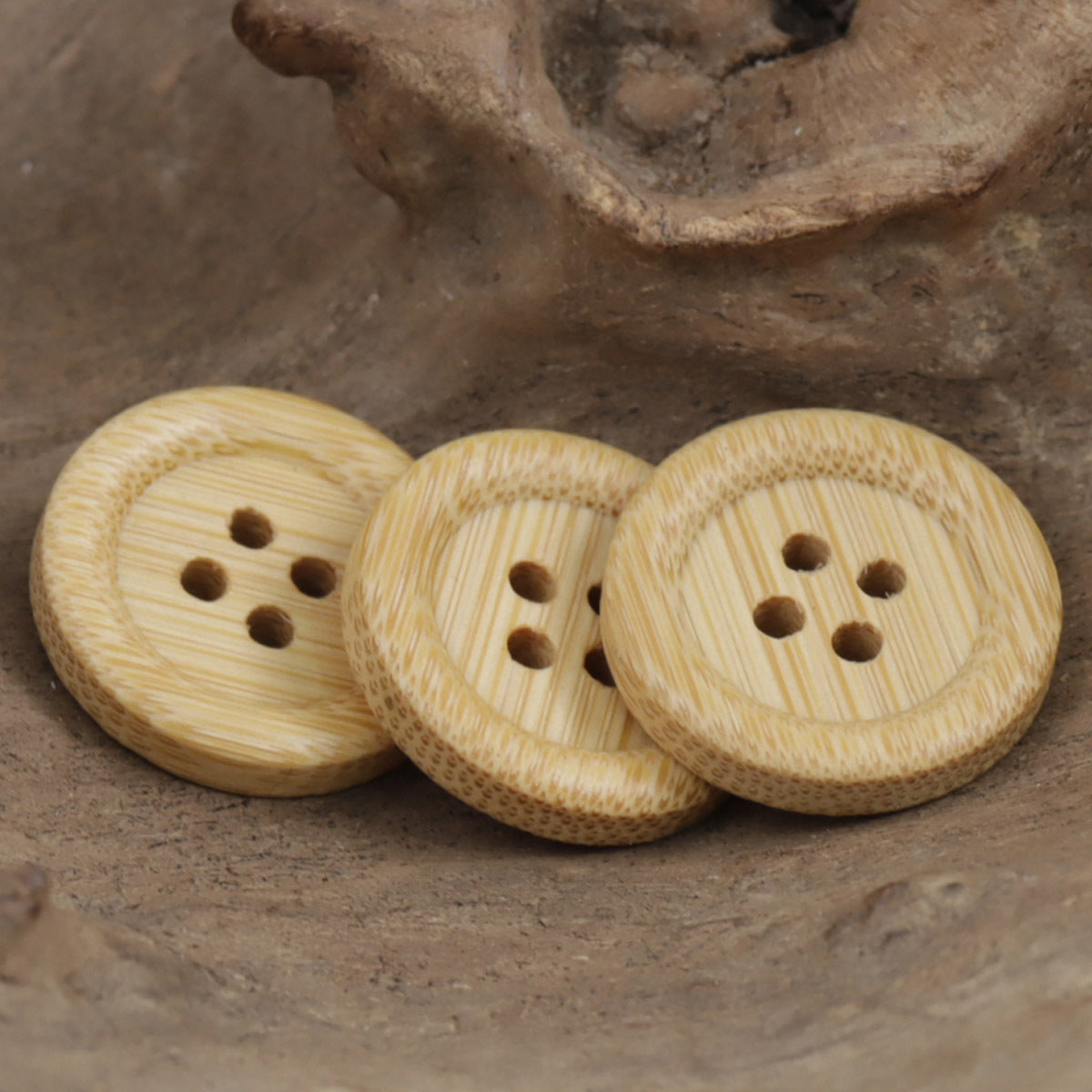 Three light tan bamboo buttons with four holes and striped wood grain