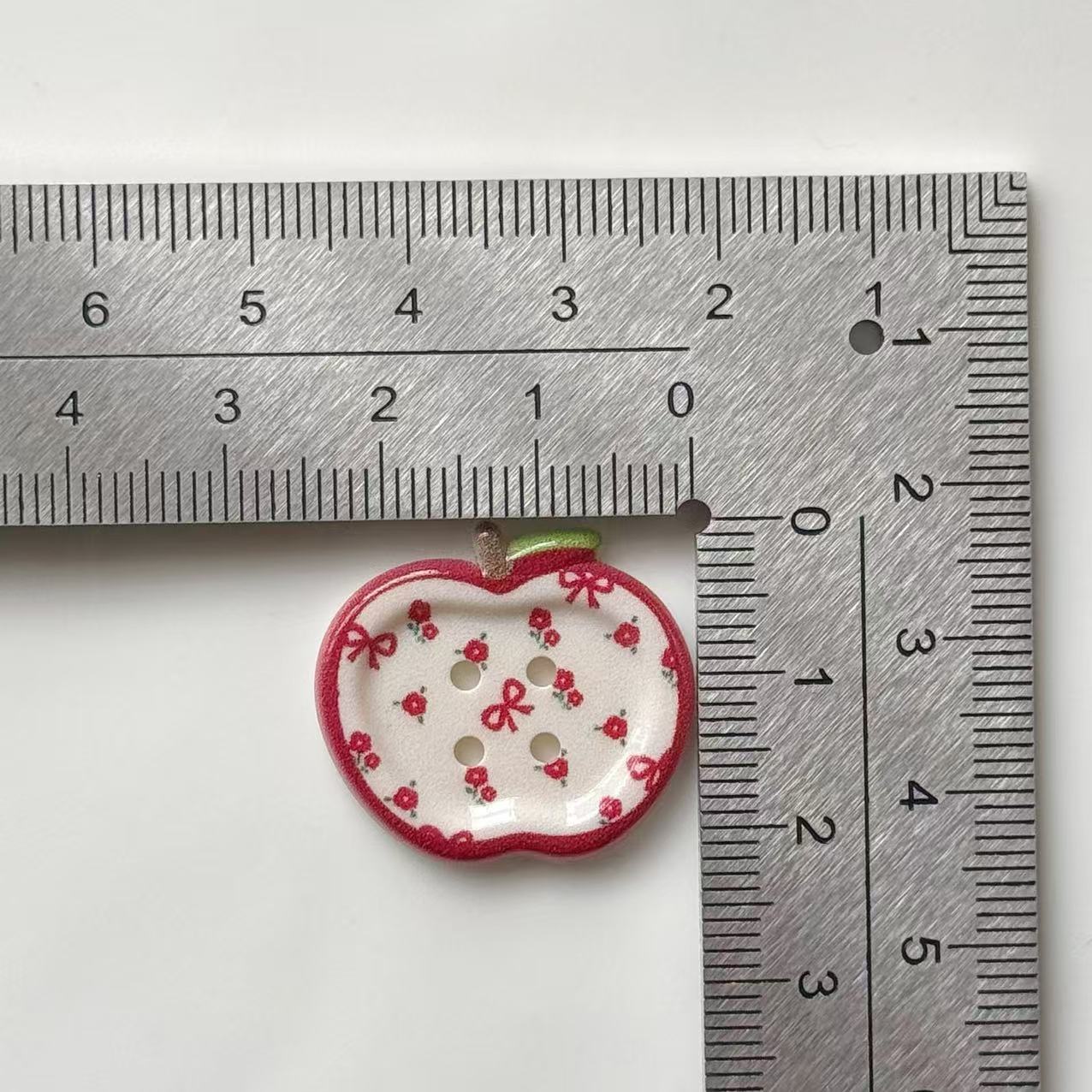 25 mm apple resin button with red floral print, 4-hole, shown against ruler
