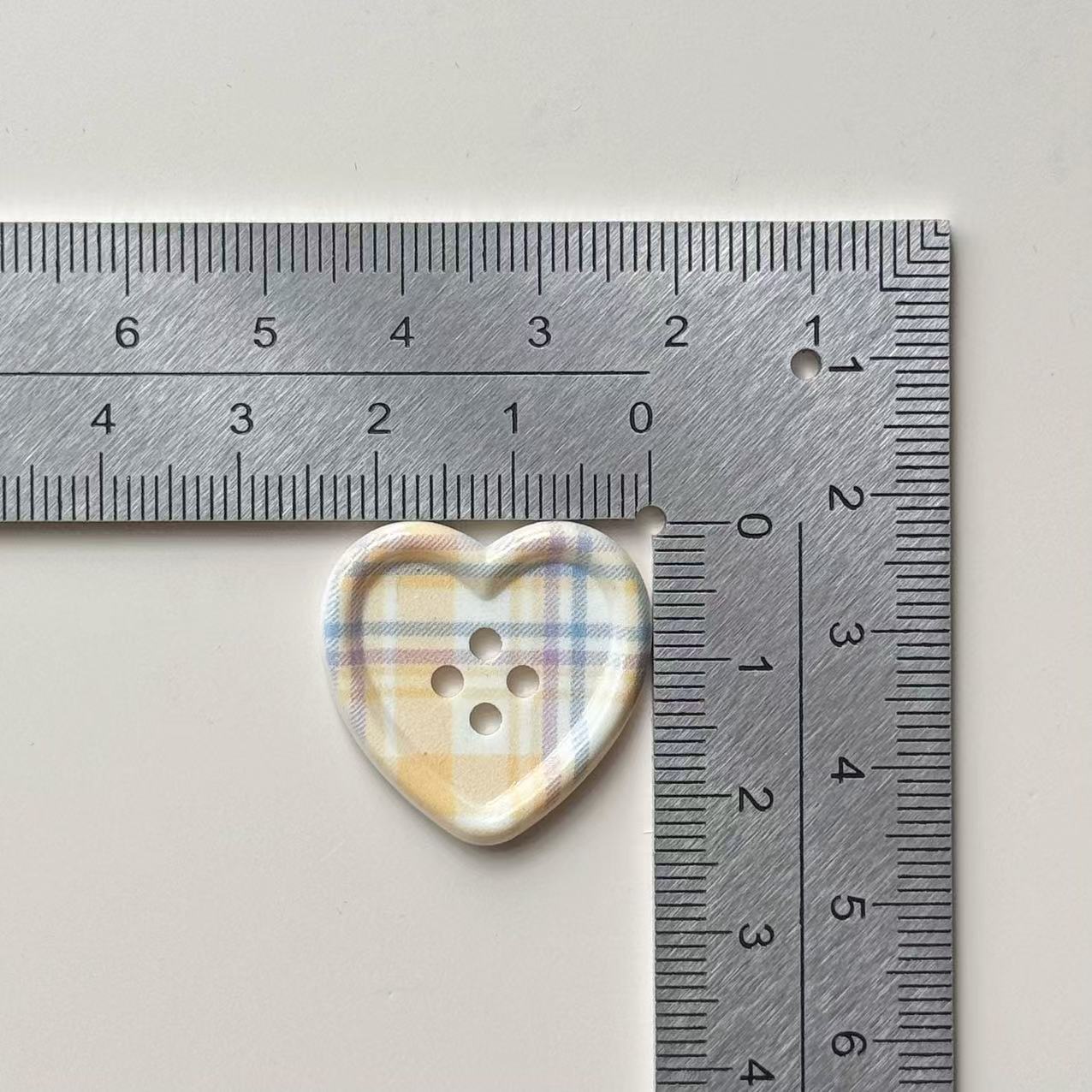 25mm tartan heart button with four holes, cream plaid; size shown with ruler