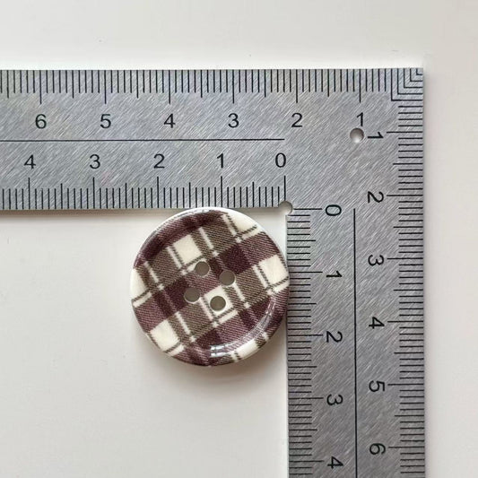 1-inch round 4-hole button with coffee plaid design, shown next to ruler