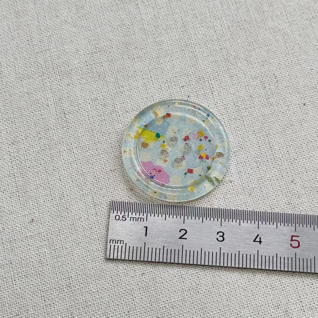 Botón resina 25 mm rosa brillante, 4 agujeros, redondo, transparente con confeti amarillo y morado