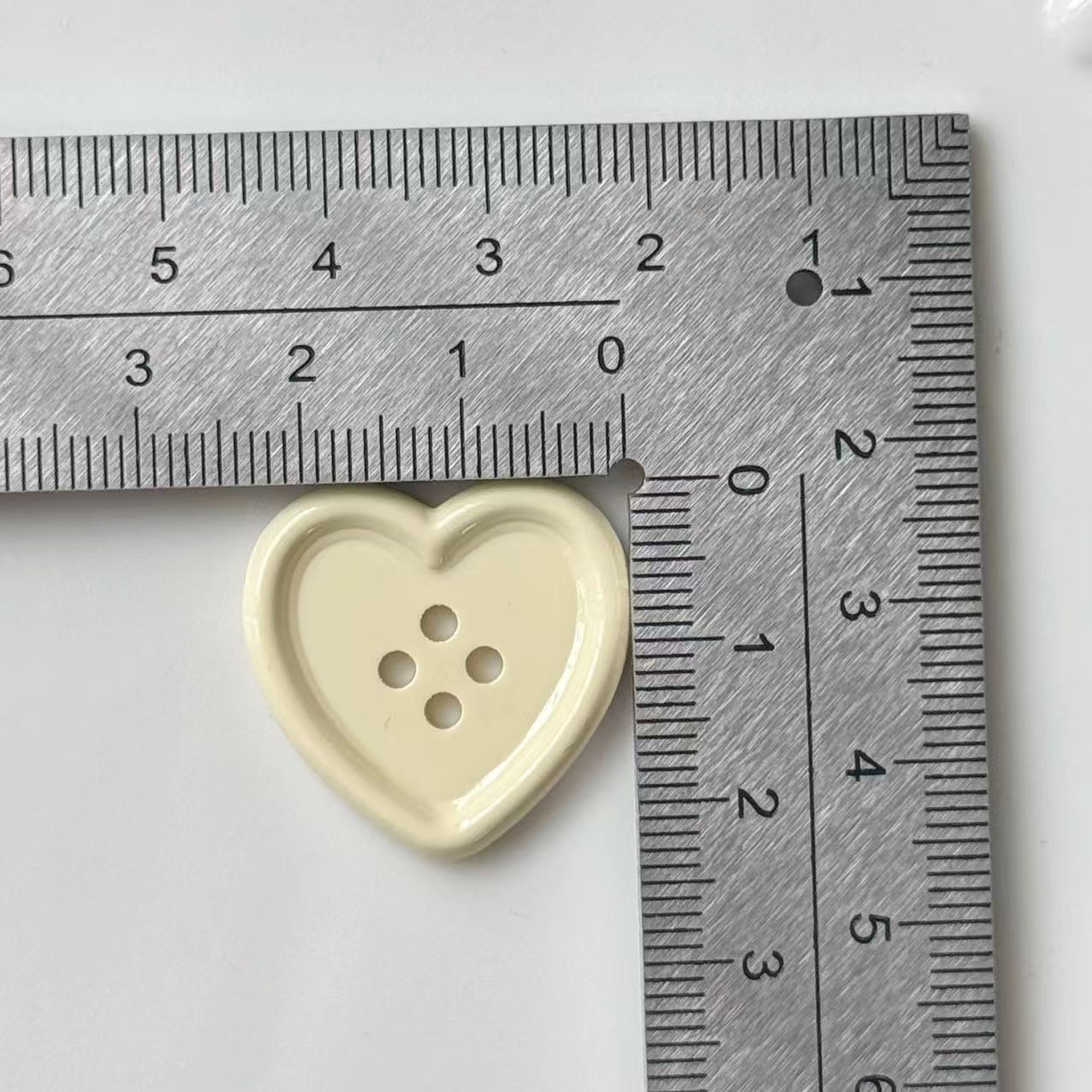 25mm shiny beige heart button, plastic, with 4-hole center shown beside ruler