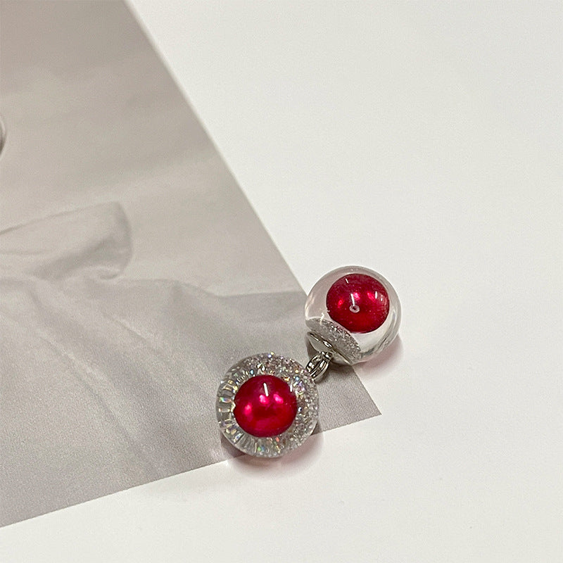 Ruby-red round pearl-style button with glittery silver rim and metal loop