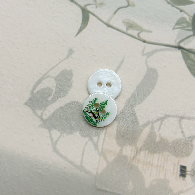 Two-hole shell button with green deer and pine branch motif, light base
