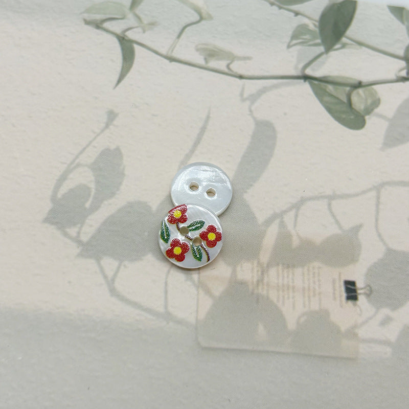 Two-hole shell button with red flowers and green leaves motif, light base