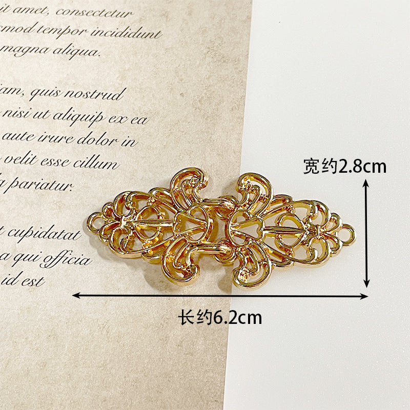 Warm gold metal frog button with intricate filigree scrolls and decorative fastening loops