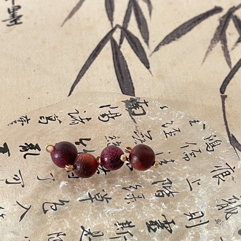 Burgundy round wooden bead charms with gold loops and small dark wooden caps.