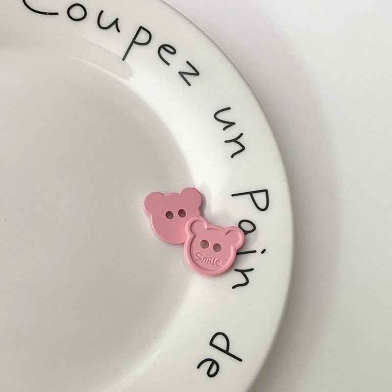 Pink cartoon teddy bear face plastic buttons, each with two holes and “Smile”