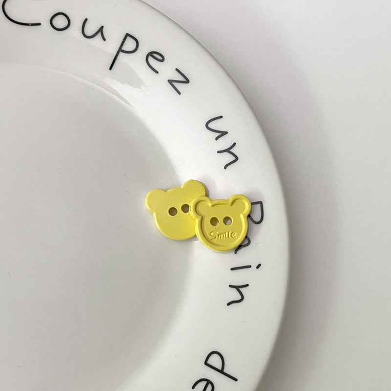 Yellow cartoon teddy bear face plastic buttons, each with two holes and “Smile”