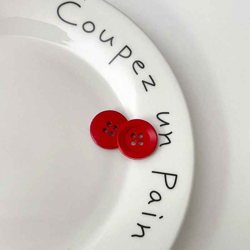 Two four-hole circular plastic buttons in red for children’s clothing