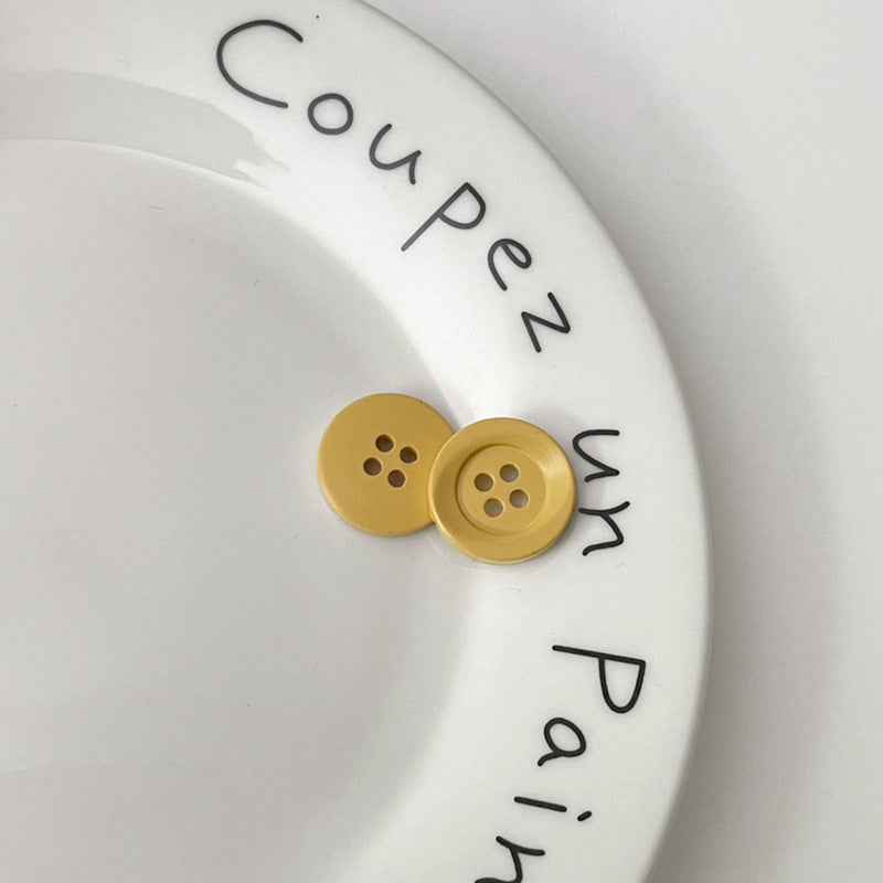 Two four-hole circular plastic buttons in mustard yellow for children’s clothing