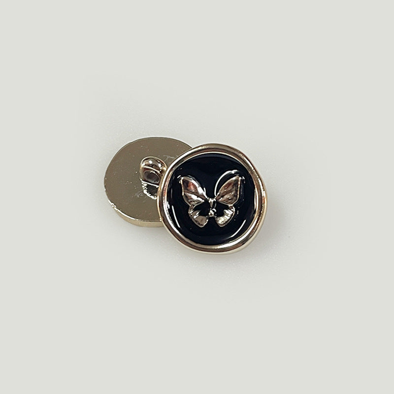 Round black plastic shank button with butterfly emblem and metal back loop