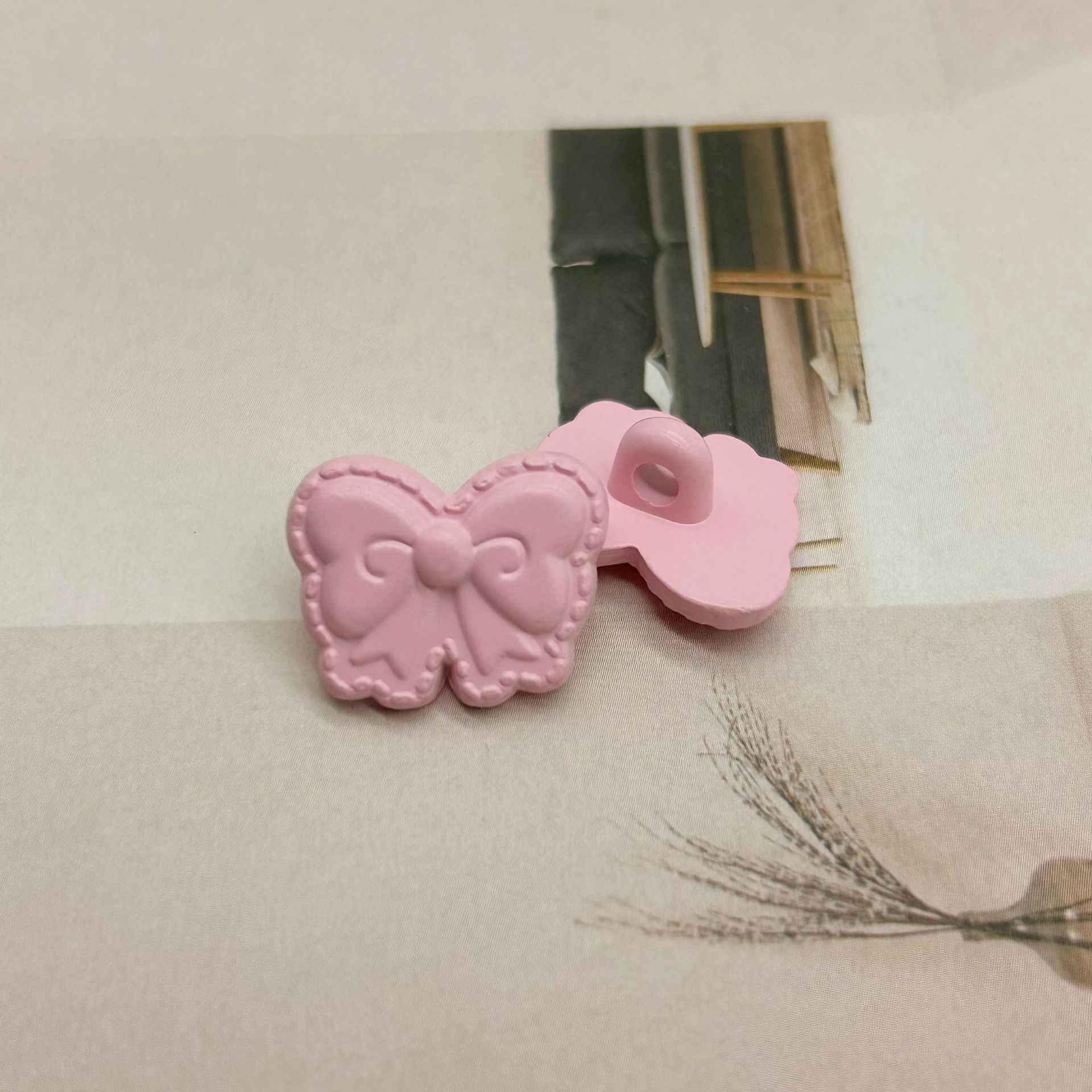 Pink butterfly-shaped shank buttons with bow detail, one back with sewing loop