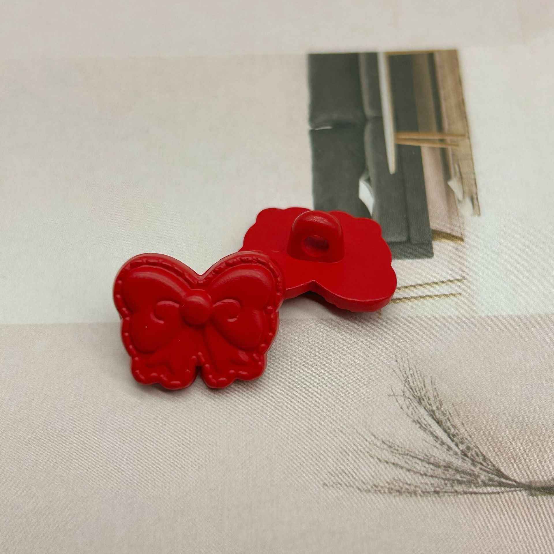 Red butterfly-shaped shank buttons with bow detail, one shows sewing loop