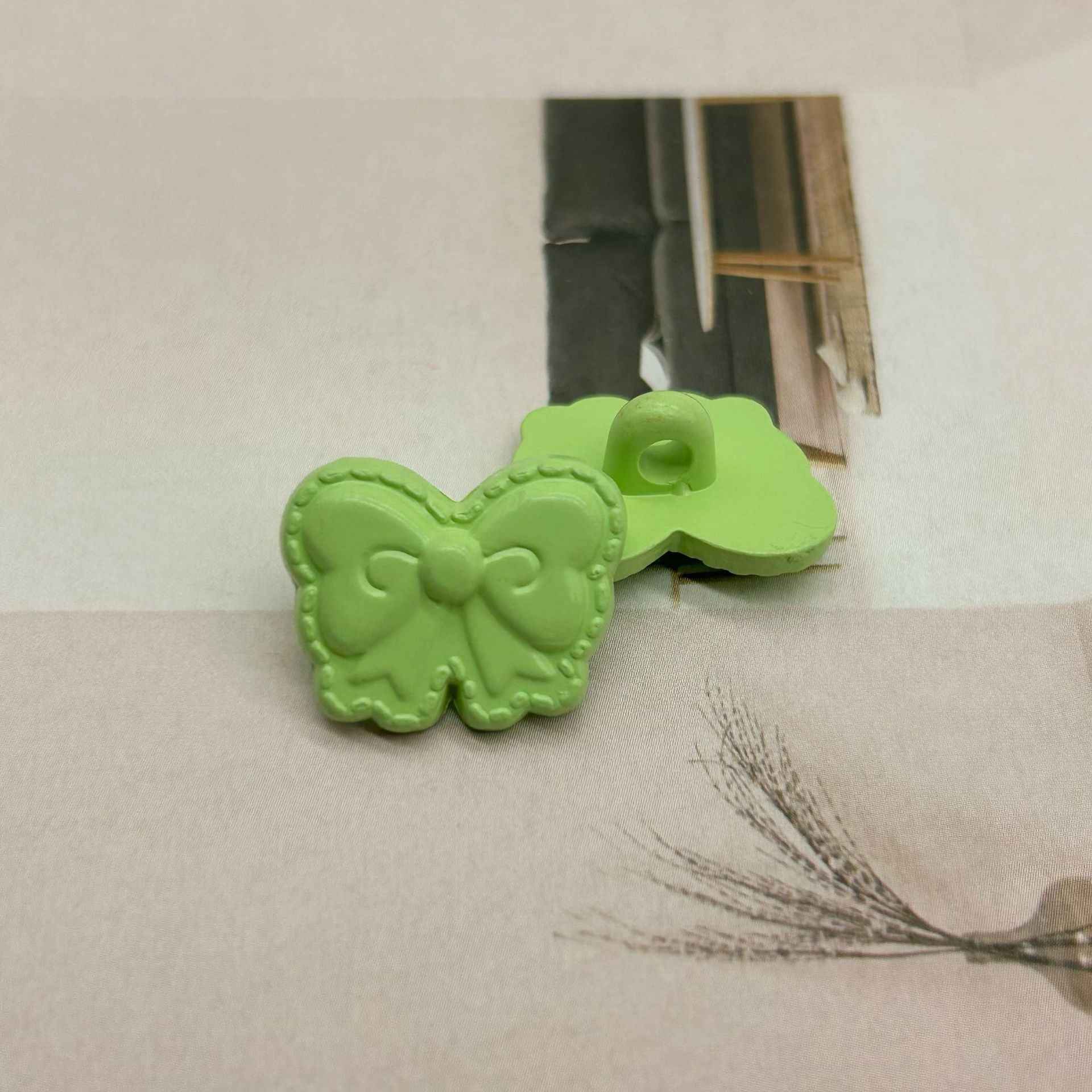 Green butterfly-shaped shank buttons with bow detail, side view