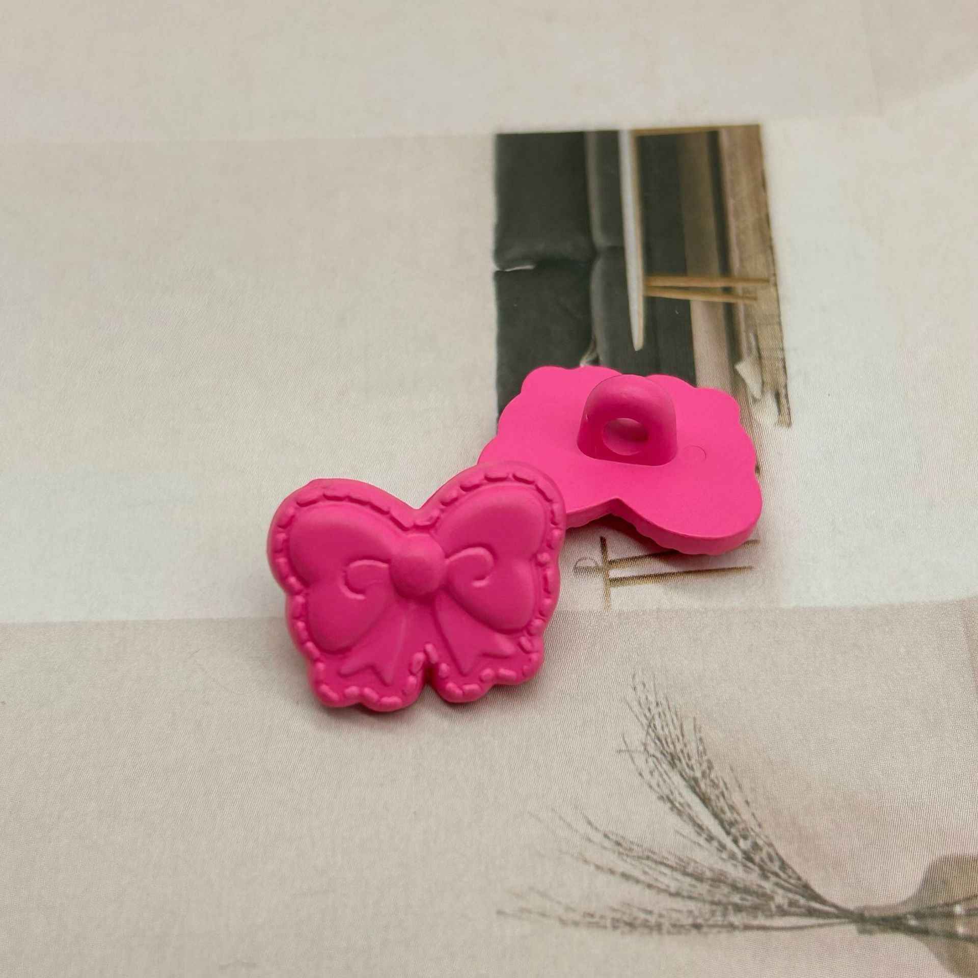 Hot pink butterfly-shaped shank buttons with bow detail, sewing loop visible