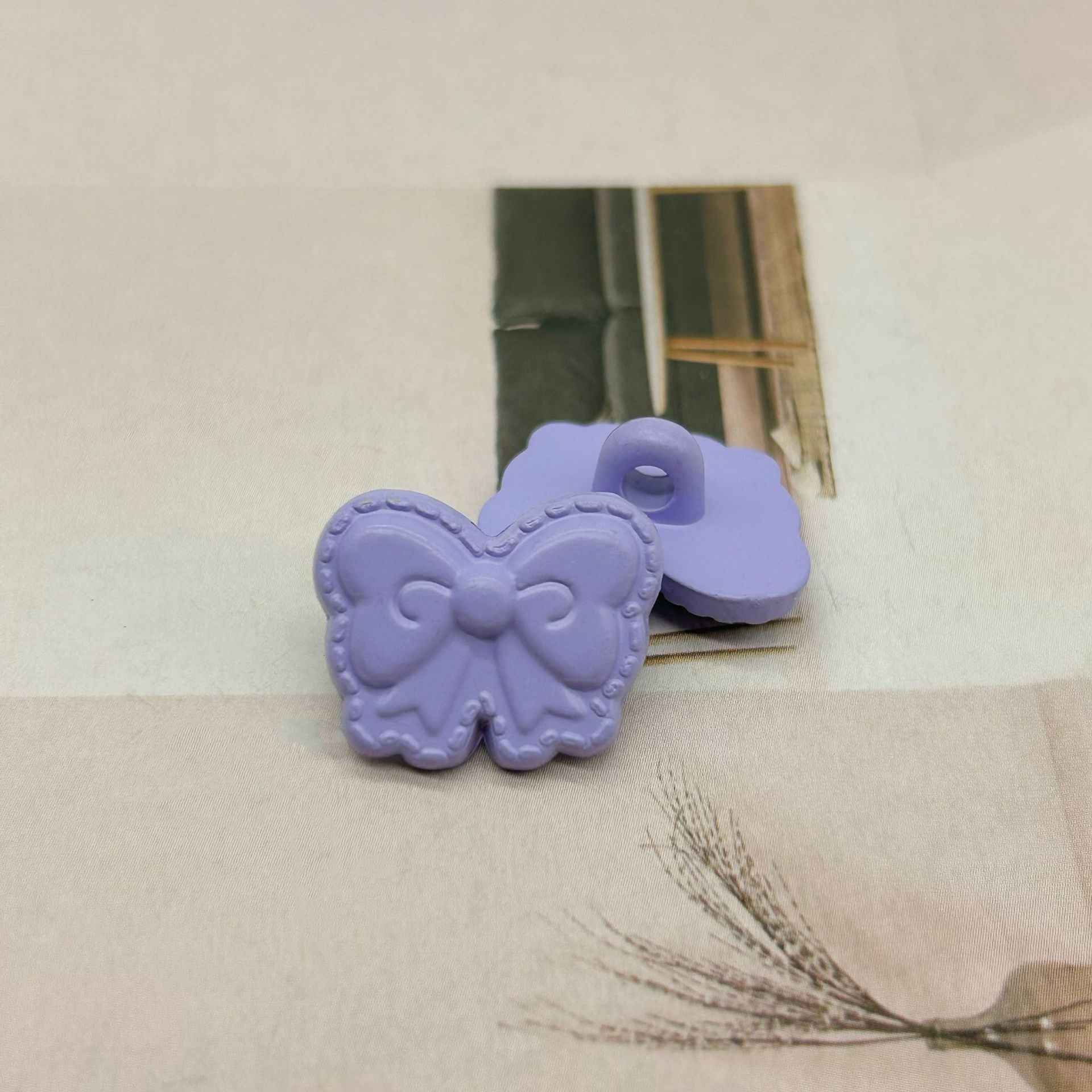Lilac butterfly-shaped shank buttons with bow detail, one button with loop