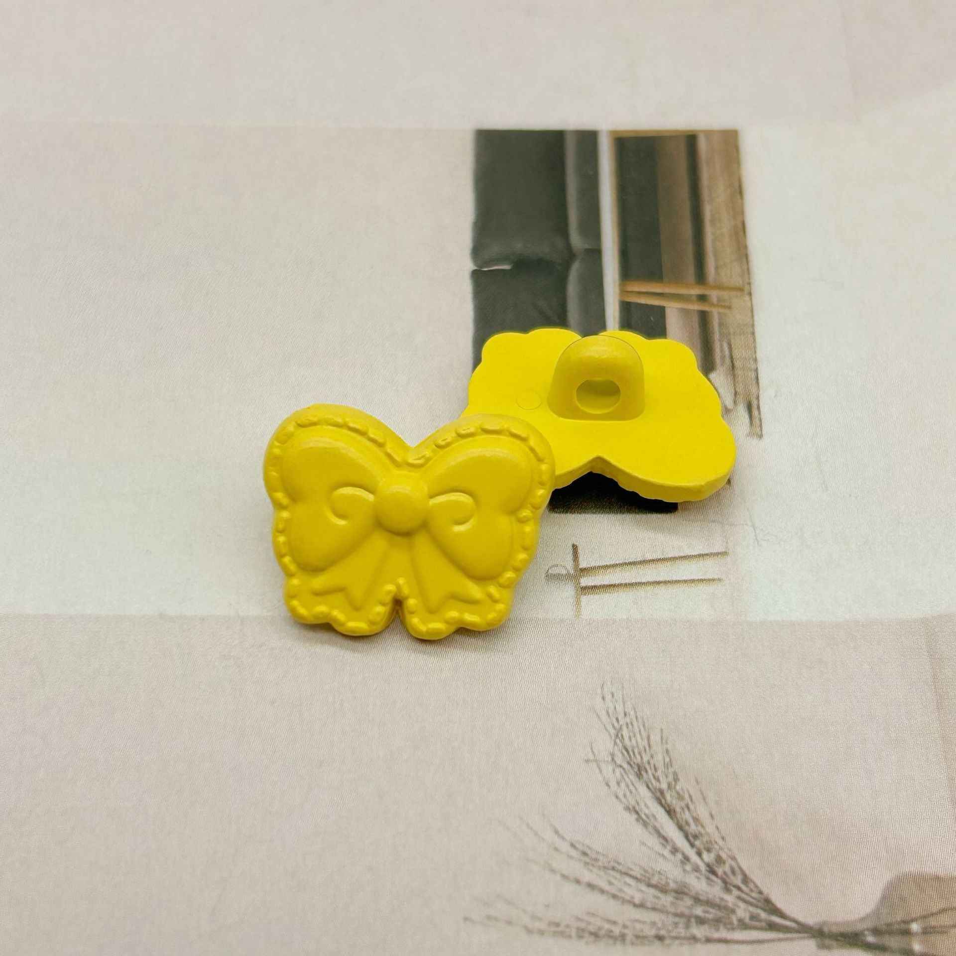 Yellow butterfly-shaped shank buttons with bow detail, one shows button hole