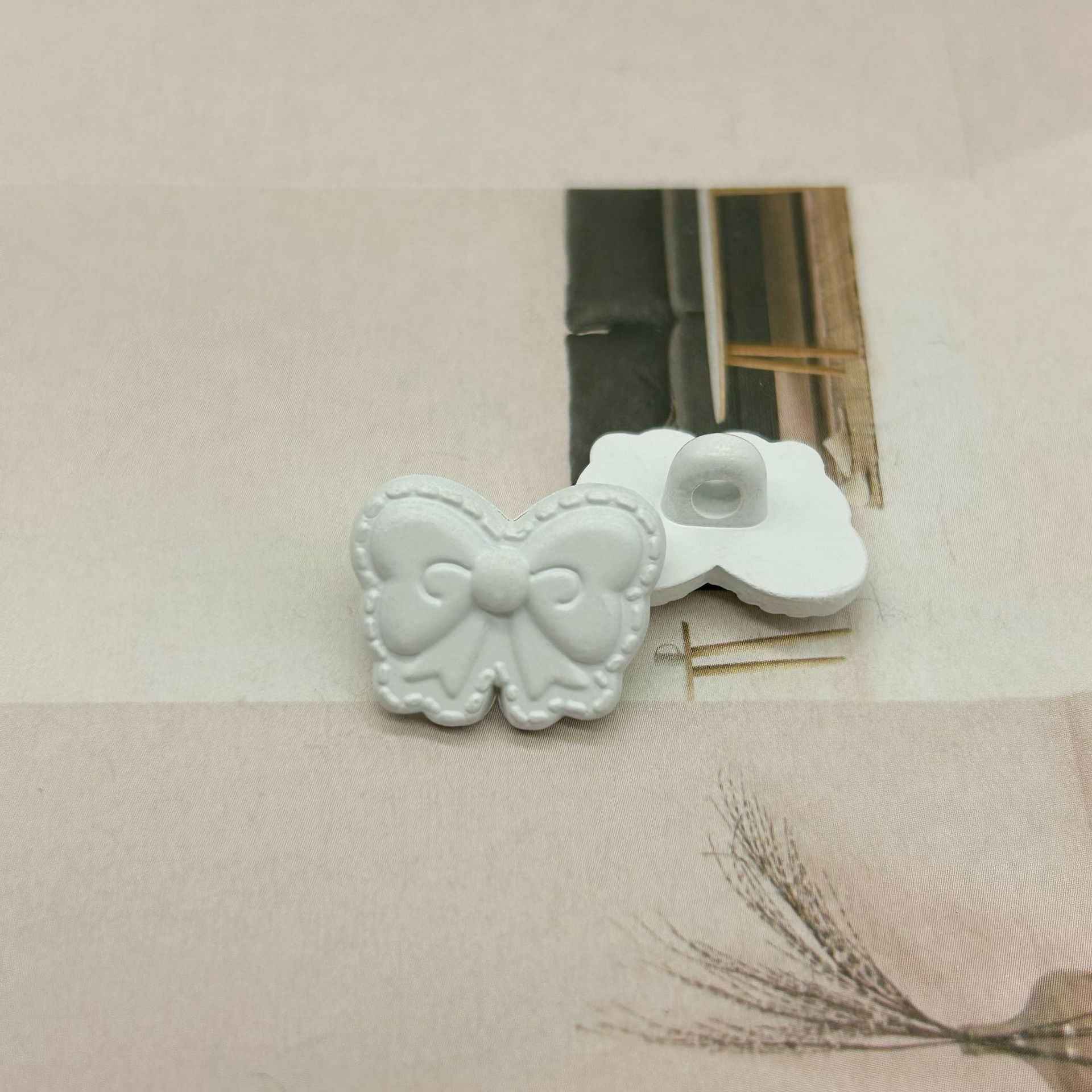White butterfly-shaped shank buttons with bow detail, loop visible on one