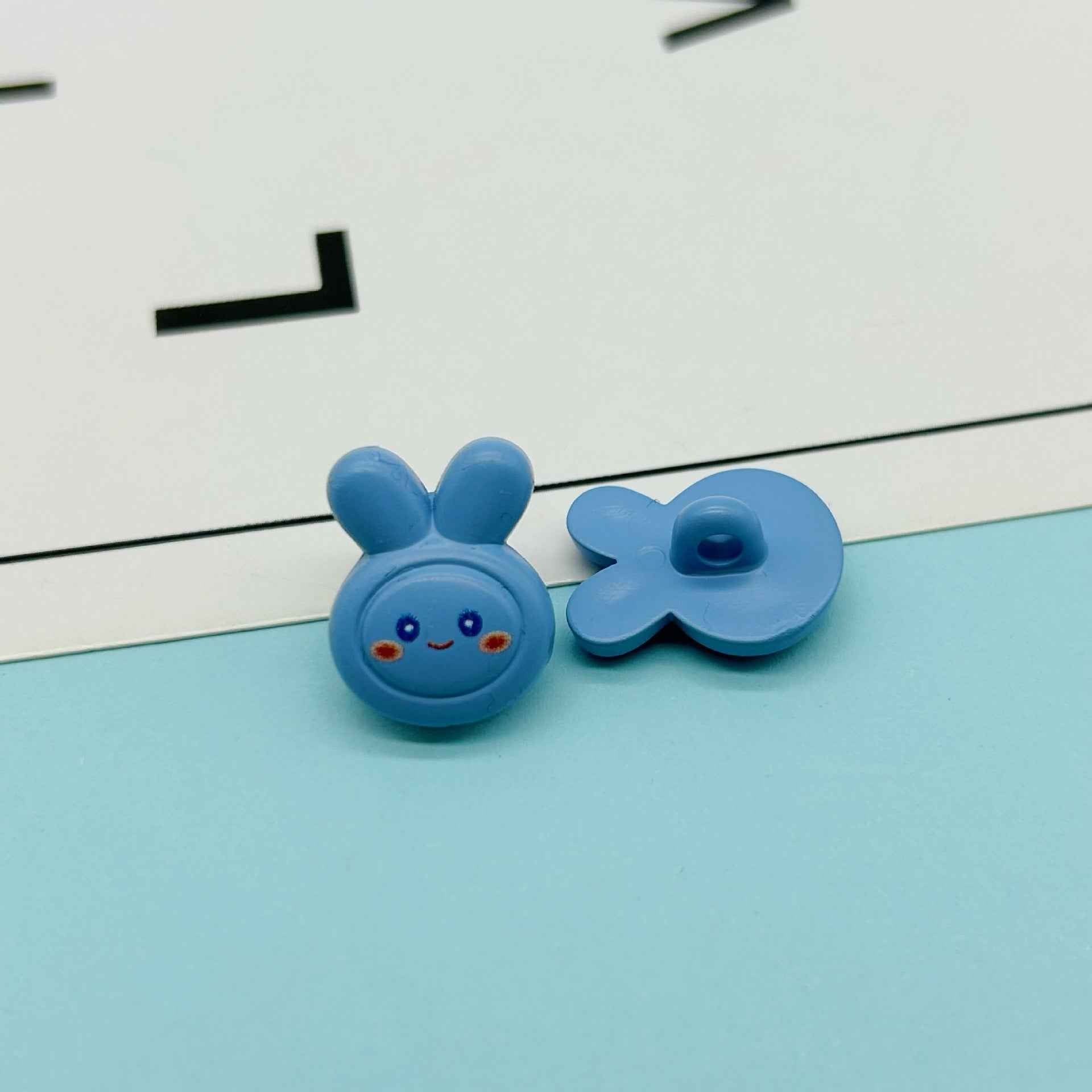 Blue cartoon rabbit button pair: bunny face with ears and flower-shaped bow button