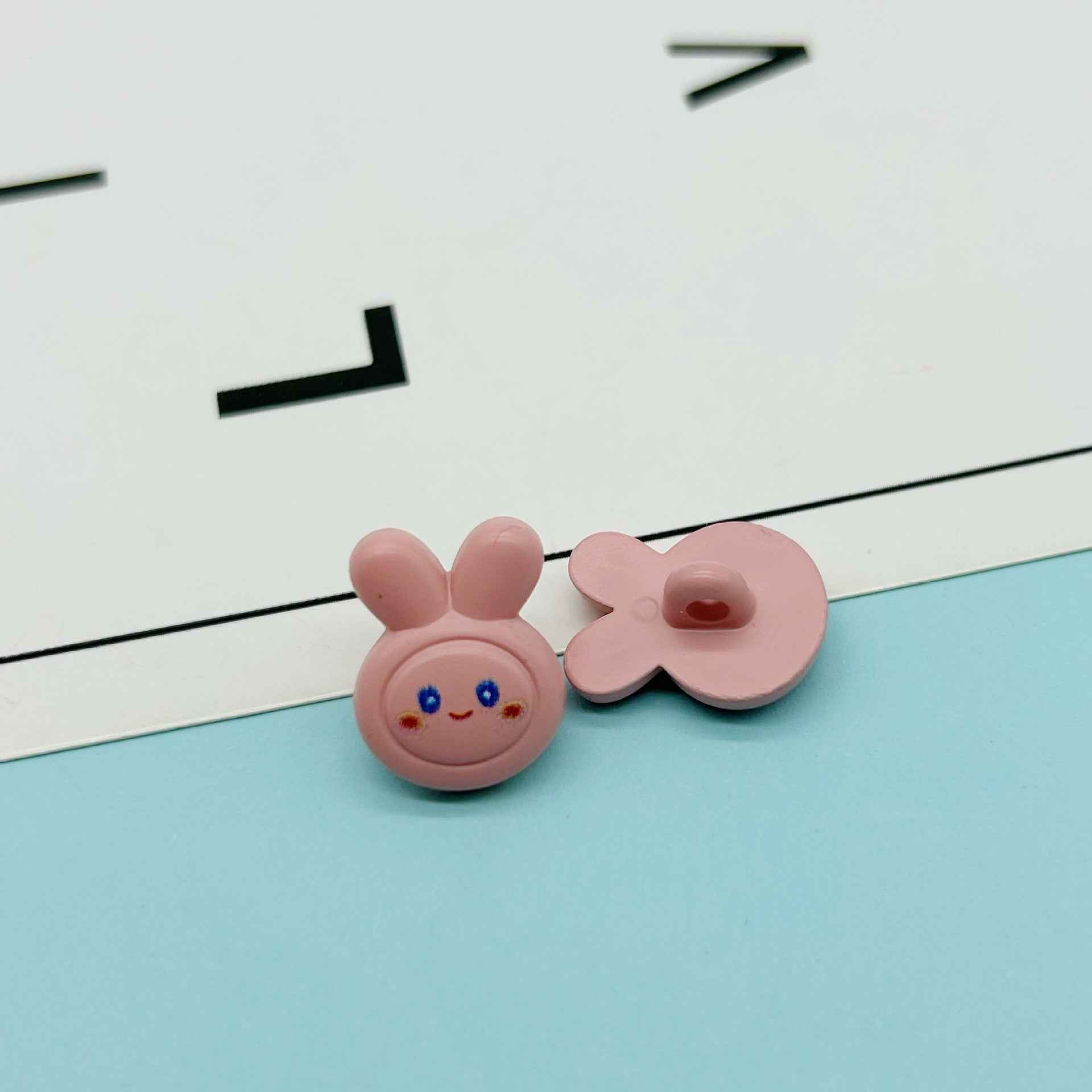 Pink cartoon rabbit buttons: bunny face with two ears and matching bow-like button