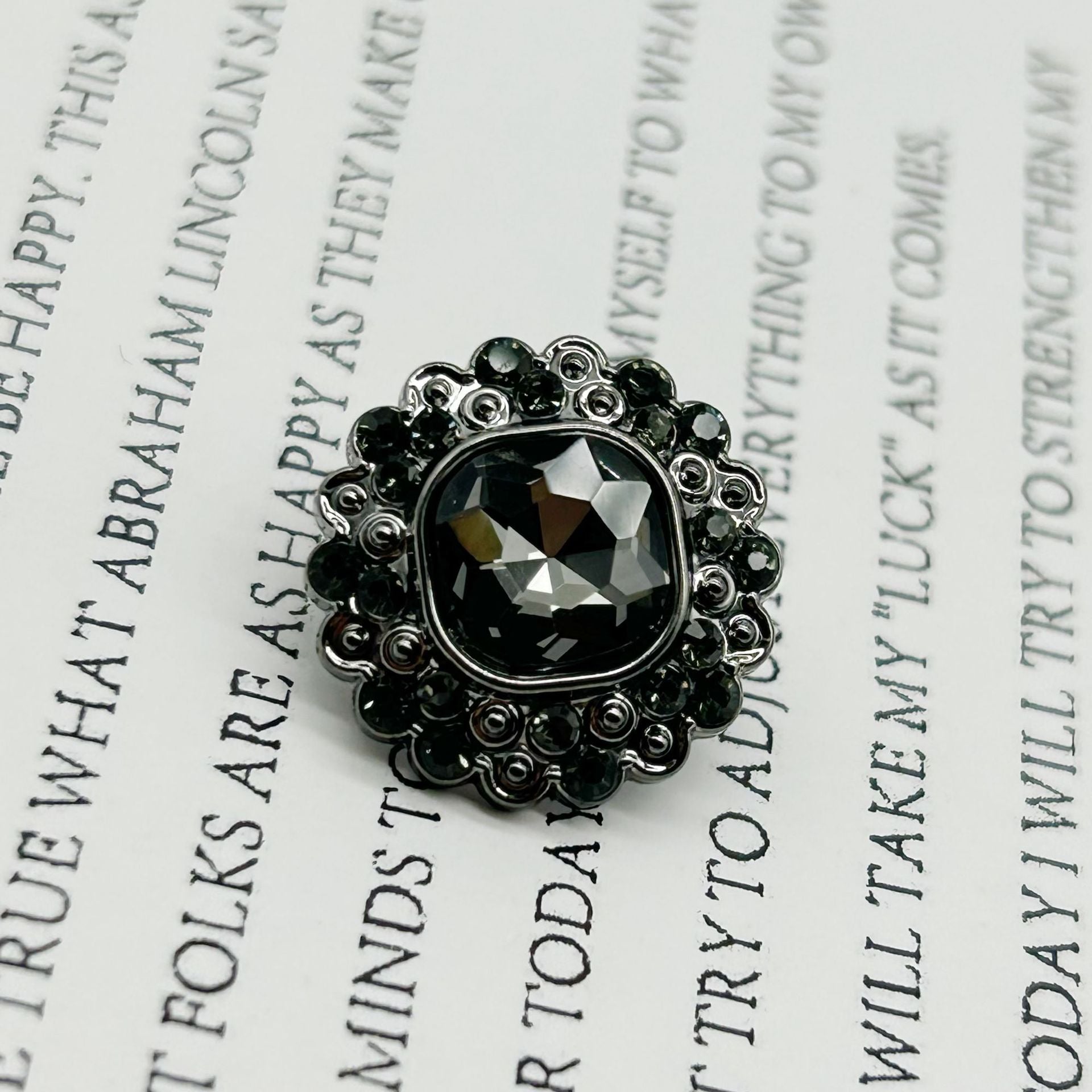 Gunmetal-tone diamond-flower shank button, dark faceted center on ornate plastic.