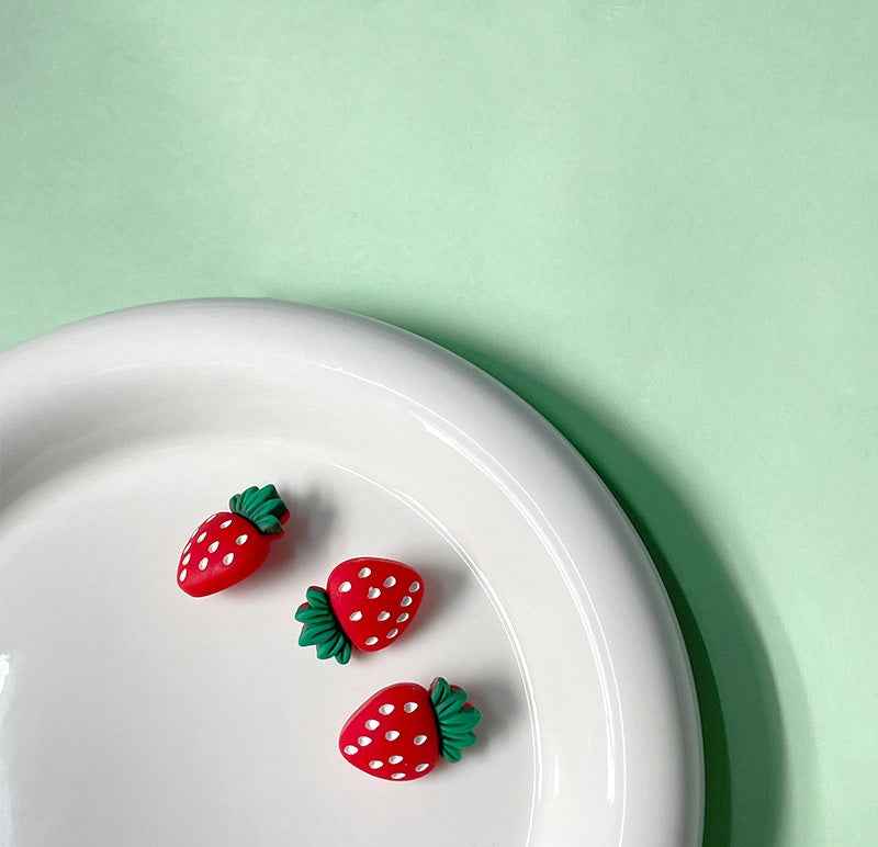 Three red strawberry buttons with green tops and white spots on plate