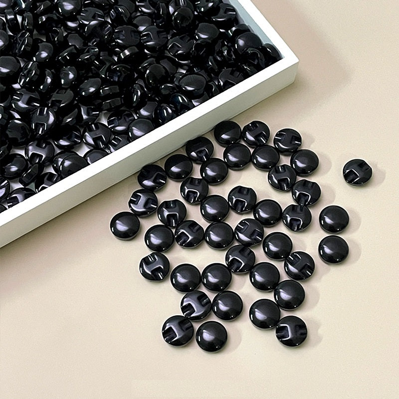 Black resin concealed-hole buttons in a tray, glossy round discs, center slot