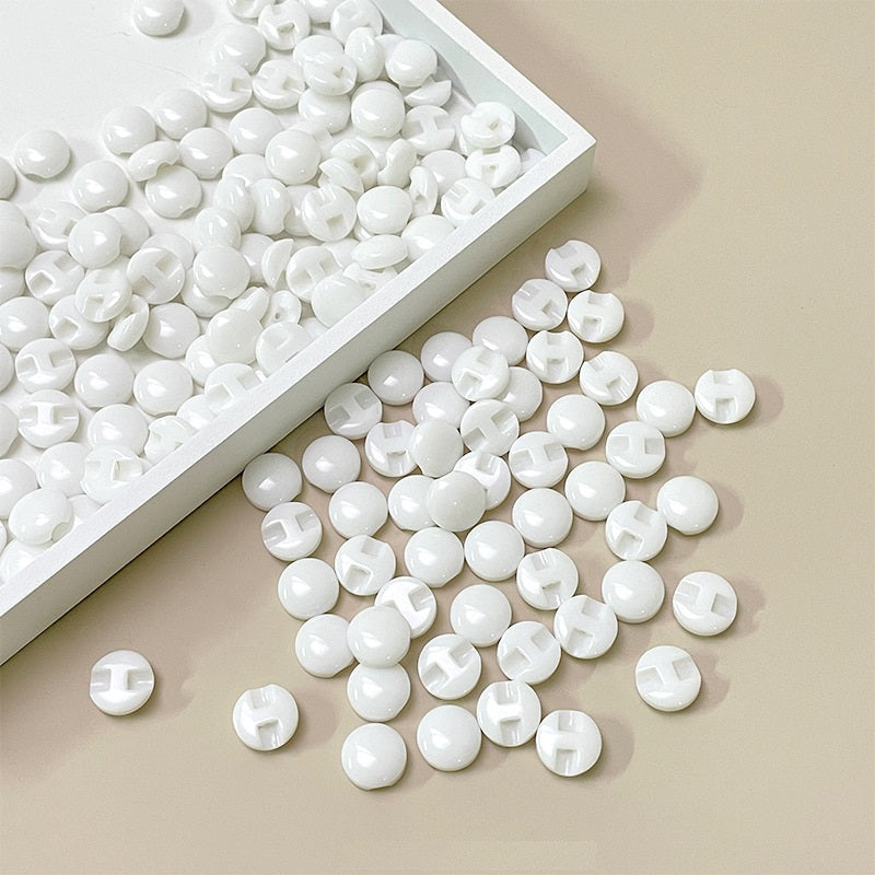White resin concealed-hole buttons in a tray, glossy round discs, center slot