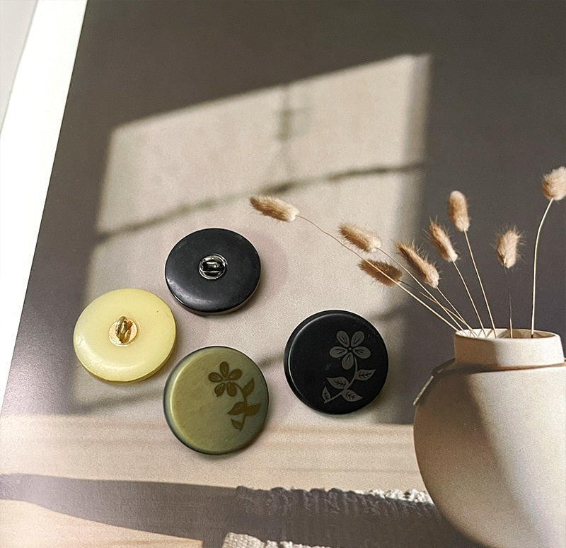 Round resin buttons with metal shanks and floral laser-cut pattern: black, white, green
