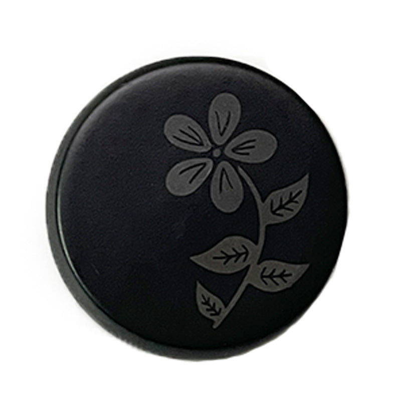 Black round resin button with laser-cut flower and leaf pattern, metal shank