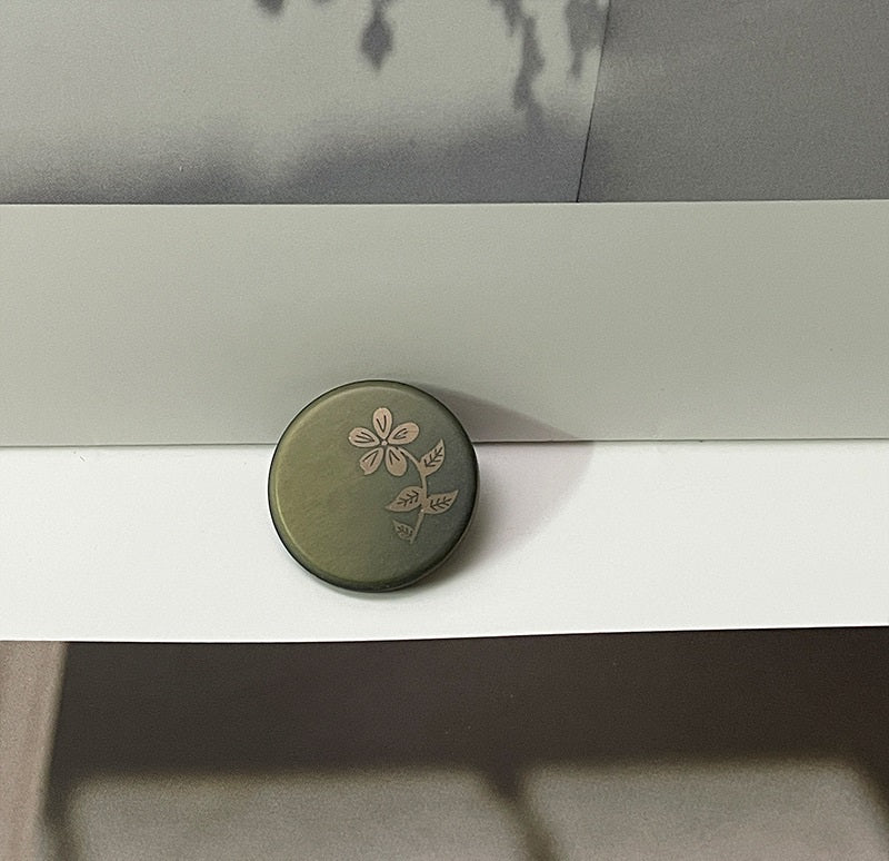 Green round resin button with laser-cut flower and leaf pattern, metal shank