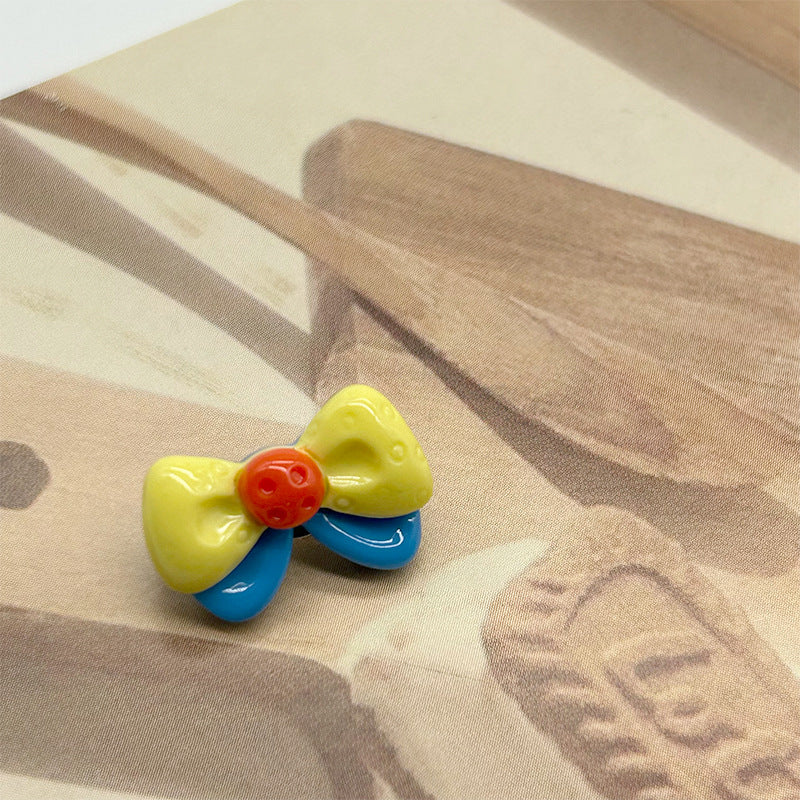 Yellow cartoon bow resin button with blue loops and red center, metal shank