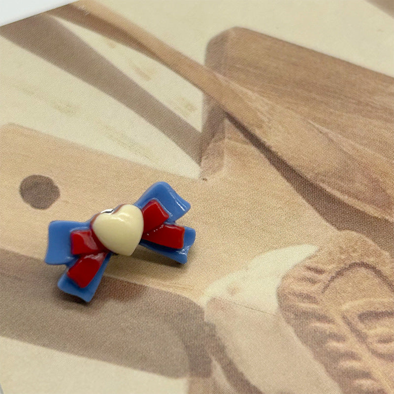 Blue cartoon bow resin button with red accents and white heart center, metal shank