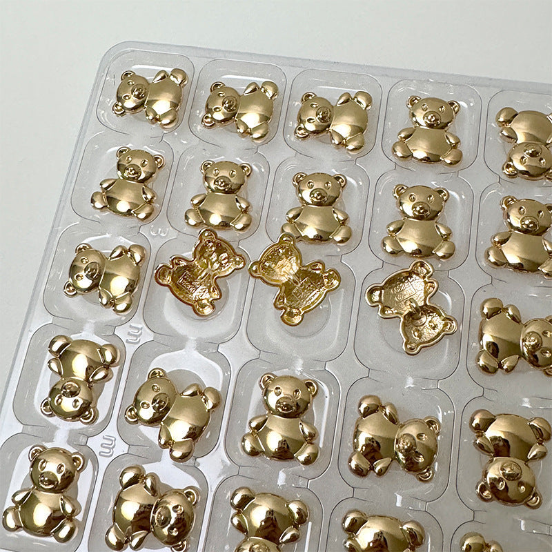 Light gold metal bear buttons in clear tray, assorted pieces in rows