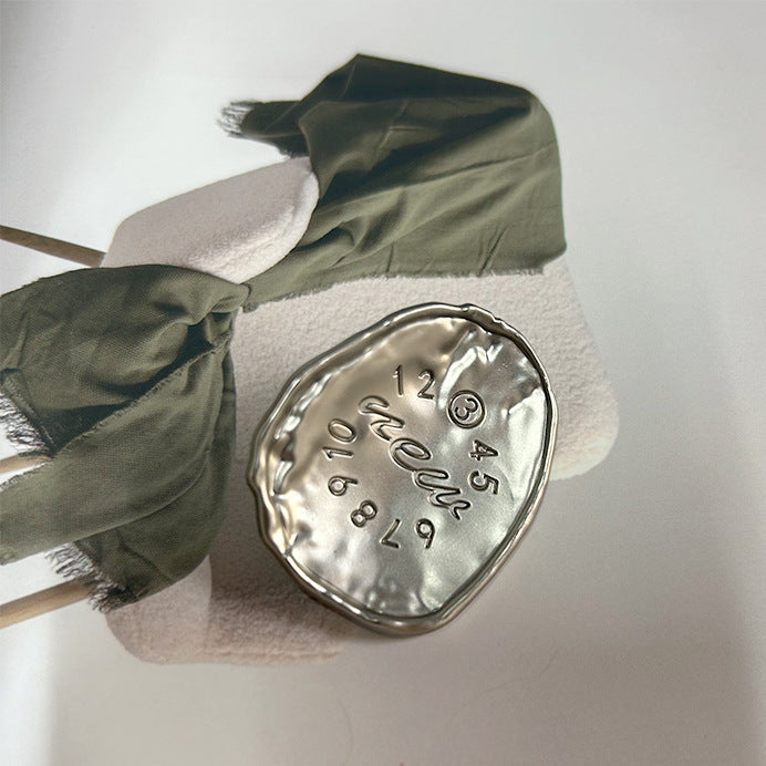 Silver oval alloy button with embossed numbers around 12 and script, shank visible