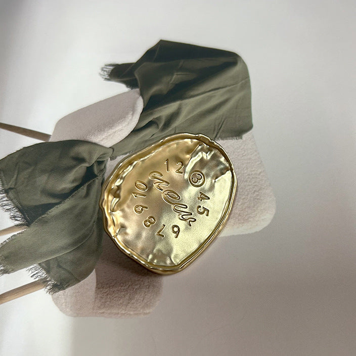 Gold oval alloy button with embossed numbers around 12 and script, shank visible