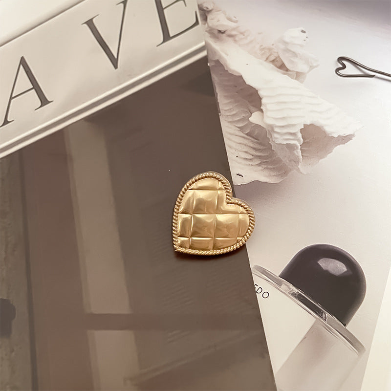 Botón corazón metálico dorado brillante con borde trenzado y relieve rectangular en la superficie